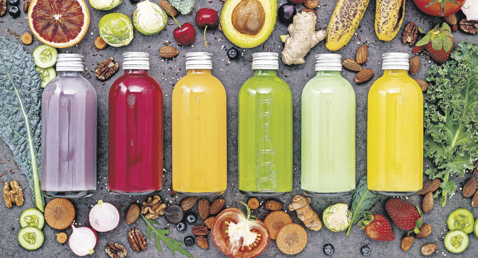 Colourful healthy smoothies and juices in bottles with fresh tropical fruit and superfoods on dark stone background with copy space.